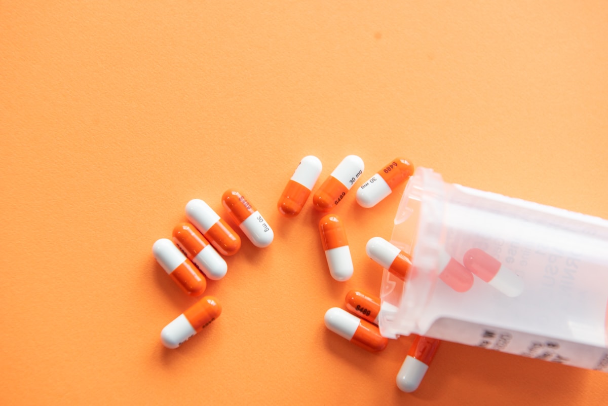 Medication spilling out of a bottle onto an orange background, representing medication administration protocols for Premier Community