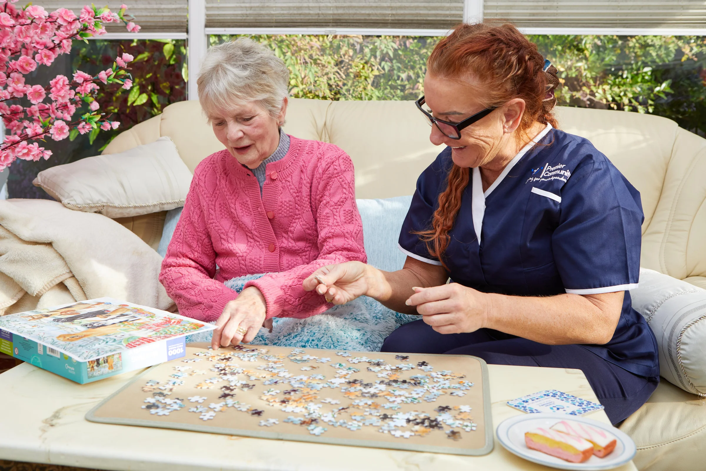 A Companionship Carer and a an elderly service user sitting on a sofa completing a jigsaw puzzle representing the benefits of companionship care