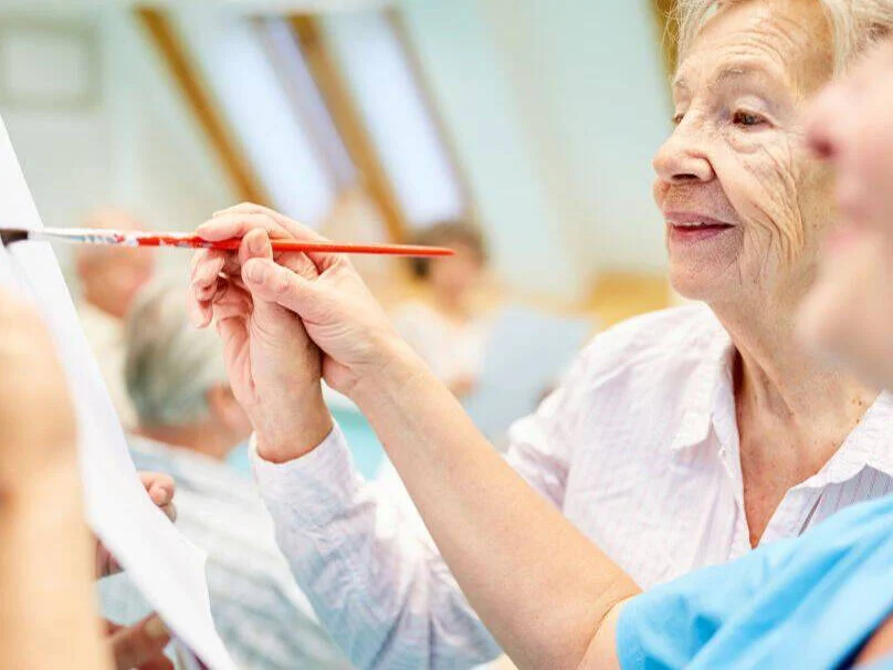 A carer helping an elderly lady to paint as part of Dementia Care