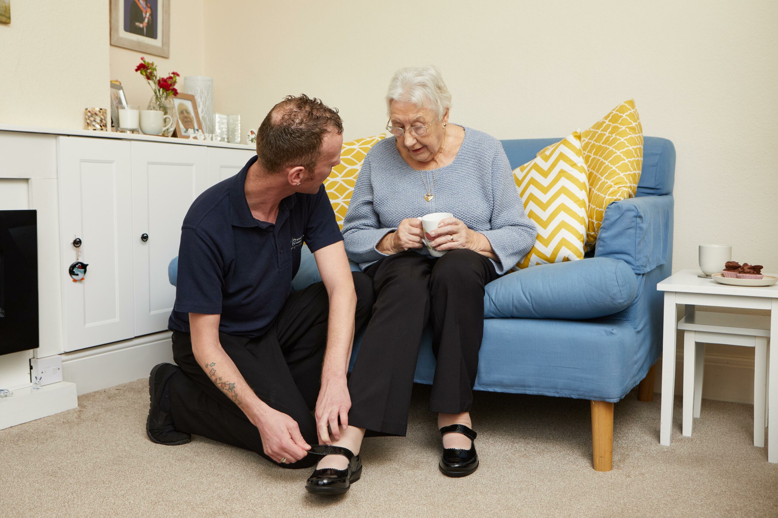 A male carer offering dressing assistance to an elderly lady by fastening her shoe