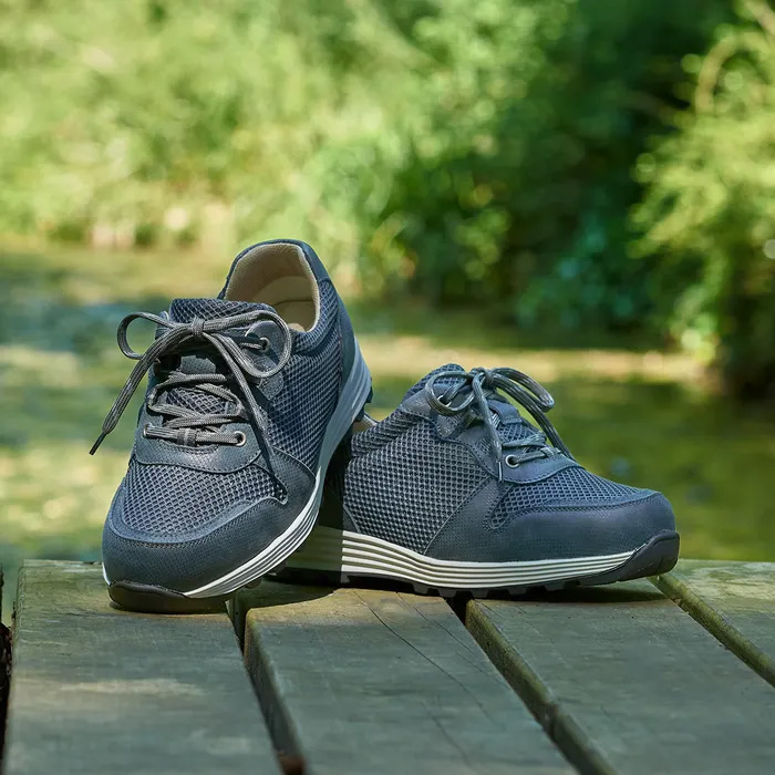A pair of Cosyfeet Misty in Sage sitting on a wooden bench with the woodland blurred behind.