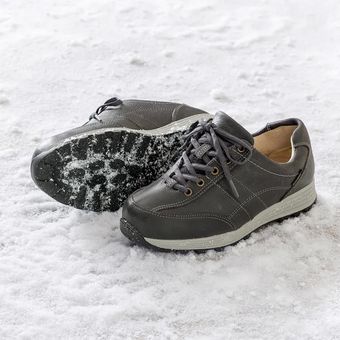 A pair of Minnie High-Performance Graphite sitting on compressed snow, one is turned over to show the sole, showing snow stuck within the sole.