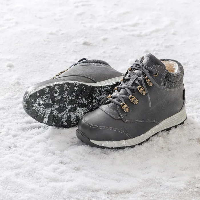 A pair of Cosyfeet Moose High-Performance Graphite sitting on the compacted snow, the right foot laying on its side showing snow stuck in the sole.