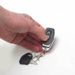 A person's hand holding the Drive 4 Wheel Autofold Scooter Key clicking the down arrow.