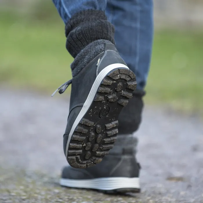 A person walking away from the camera one foot off the grown showing the sole of the Cosyfeet Moose High-Performance in Graphite.