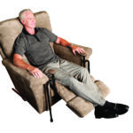 A man sitting in a large chair with the Stander EZ Stand -N- Go below the cushion underneath him.