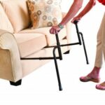 A person placing the Stander EZ Stand -N- Go below the cushion of a cream sofa.