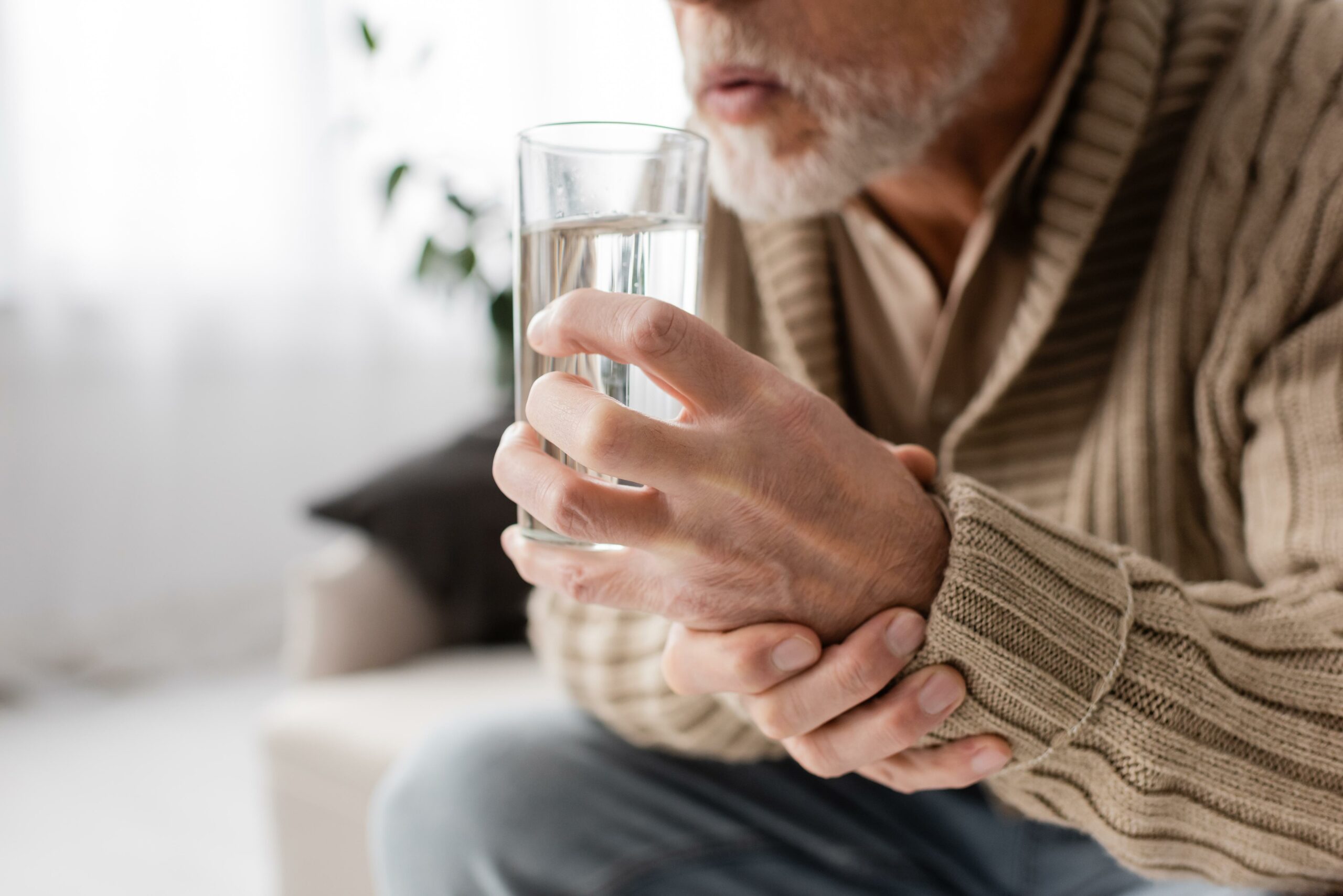 Older gentleman trying to keep his hand steady - holding a glass of water - a symptom of Parkinson's disease