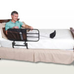 A man sitting in bed in a blue top holding onto the Stander EZ Adjustable Bed Rail