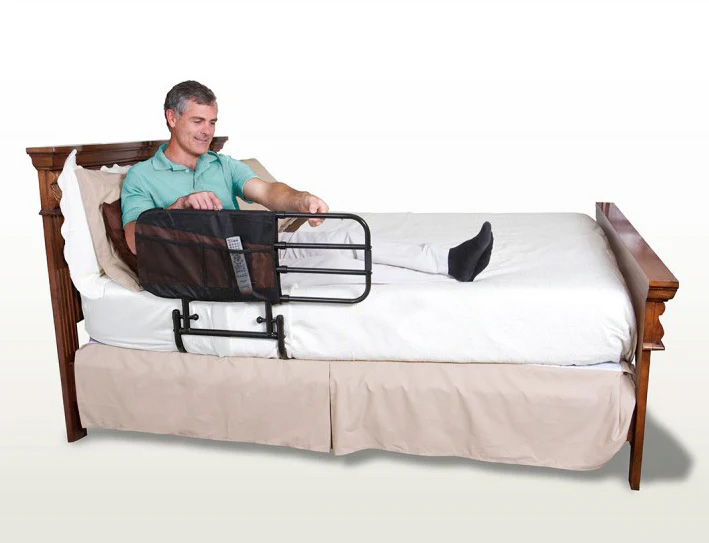 A man sitting in bed in a blue top holding onto the Stander EZ Adjustable Bed Rail