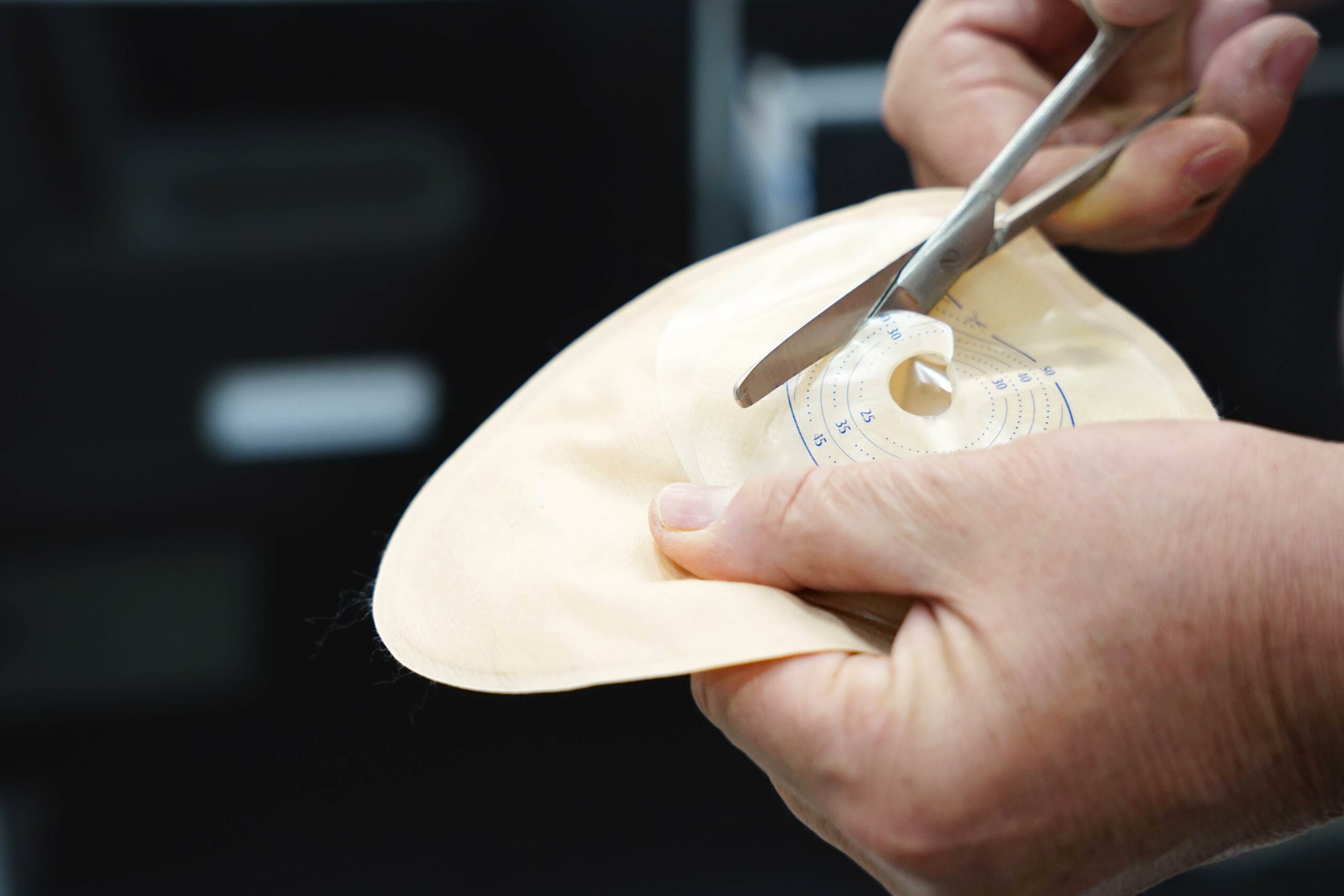 A person using scissors to adjust the opening on a stoma bag as part of a stoma care routine