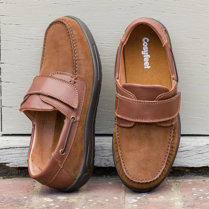 Cosyfeet Woody Tan Boat Shoes against a grey wood background and brick/tile ground.