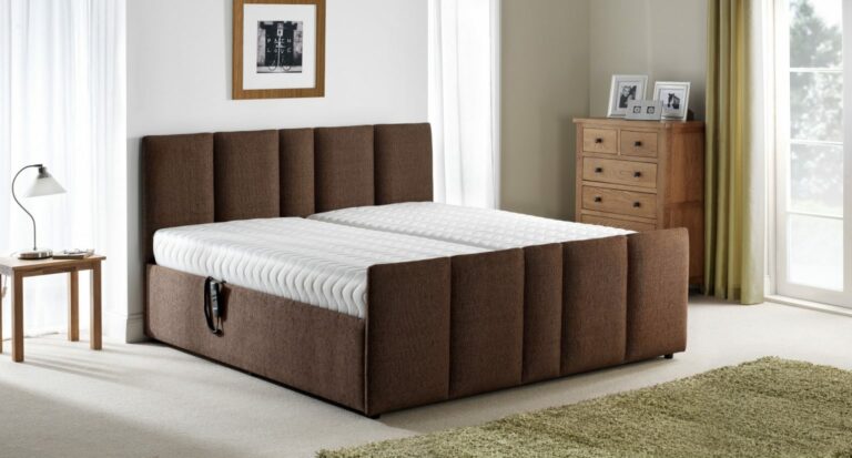 A modern bedroom features a large brown upholstered bed with a white mattress, a wooden nightstand with a lamp, a chest of drawers, and a framed picture on the wall.
