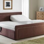 Modern bedroom with a brown adjustable bed, one side elevated. Soft lighting, a wooden nightstand, and a dresser create a cozy and serene atmosphere.