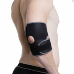 A topless male, stood side on from the camera, facing right, with his right arm down his side wearing the Kedley Advanced Elbow Support.