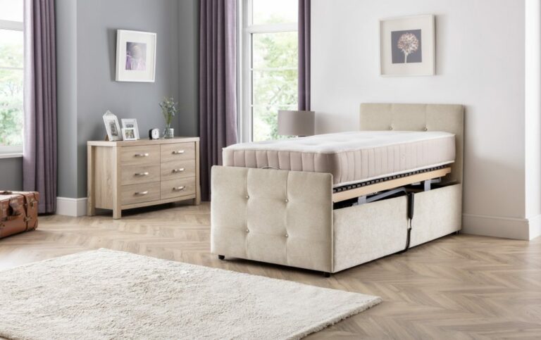 Bedroom with a neutral tone features a Custom Wiltshire Single Bed - With High Low Mech beige upholstered bed, opened to reveal storage. A light wood dresser, purple curtains, and soft decor add elegance.