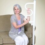 A elderly woman sitting on a sofa holding onto a Stander Security Pole & Curve Grab Bar.