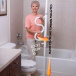 A elderly lady standing next to a toilet and bath holding onto the Stander Security Pole & Curve Grab Bar.