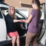 A person helping another person out of the car using the Stander Handy Handle in red.