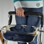 A person in a striped top and jeans holding onto the Trust Care Let's Go Indoor Yellow on a grey background.