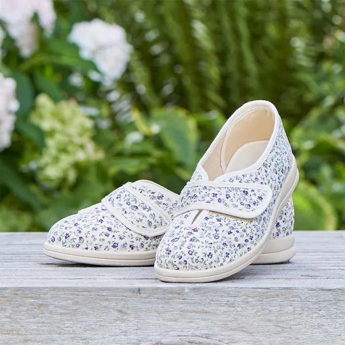 A pair of Cosyfeet Sally in Beige/Lilac Floral sitting on a stone wall which greenery blurred in the background.