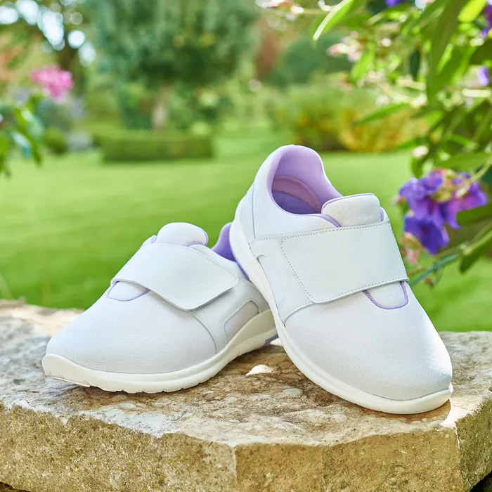 The Cosyfeet Vamos White Lilac sitting on a tree stump with a beautiful green garden behind.