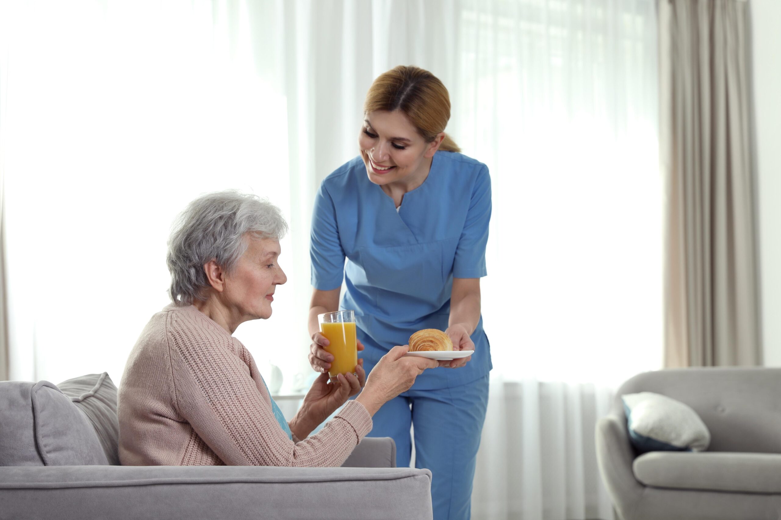 Carer handing a croissant and some orange juice to a service user in order to assist with malnutrition in the elderly