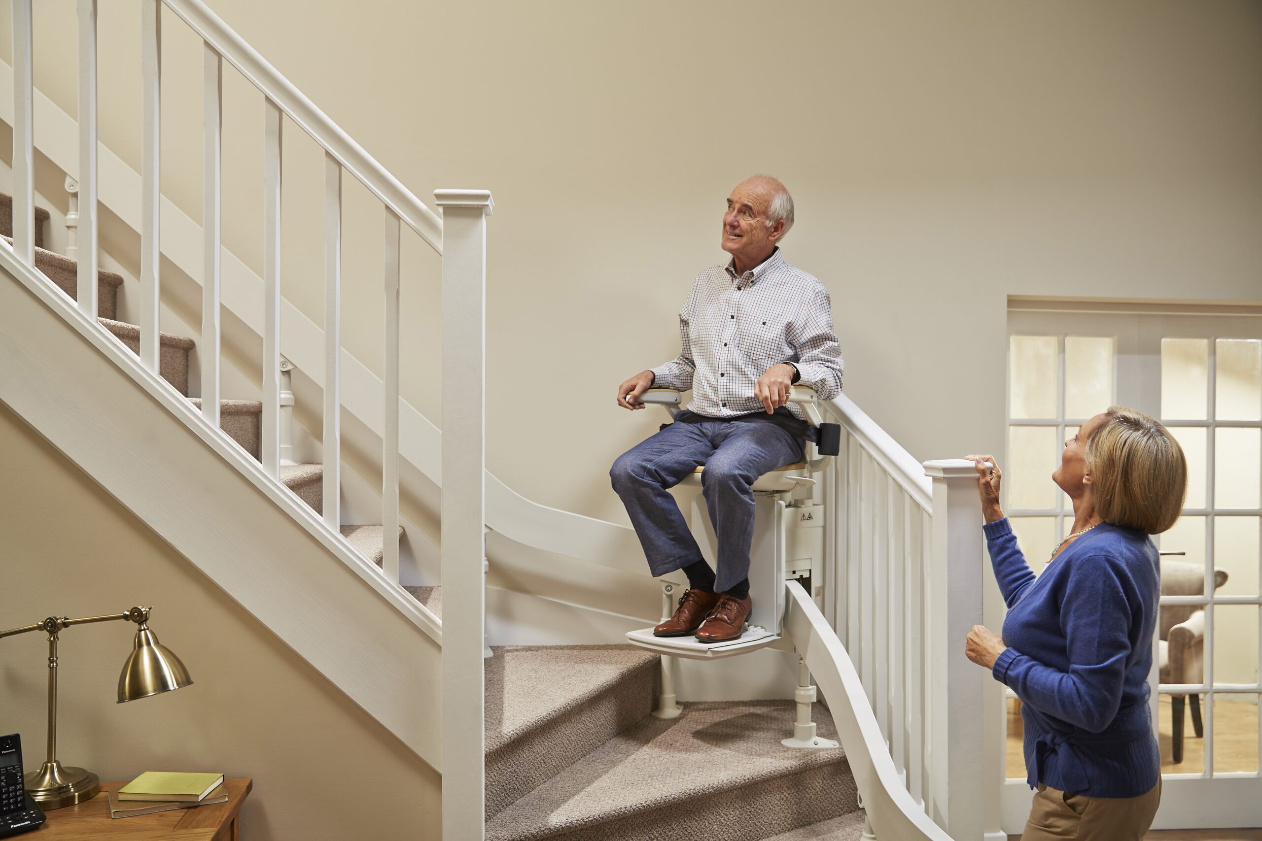 Elderly man sat on his stairlift whilst elderly woman watches