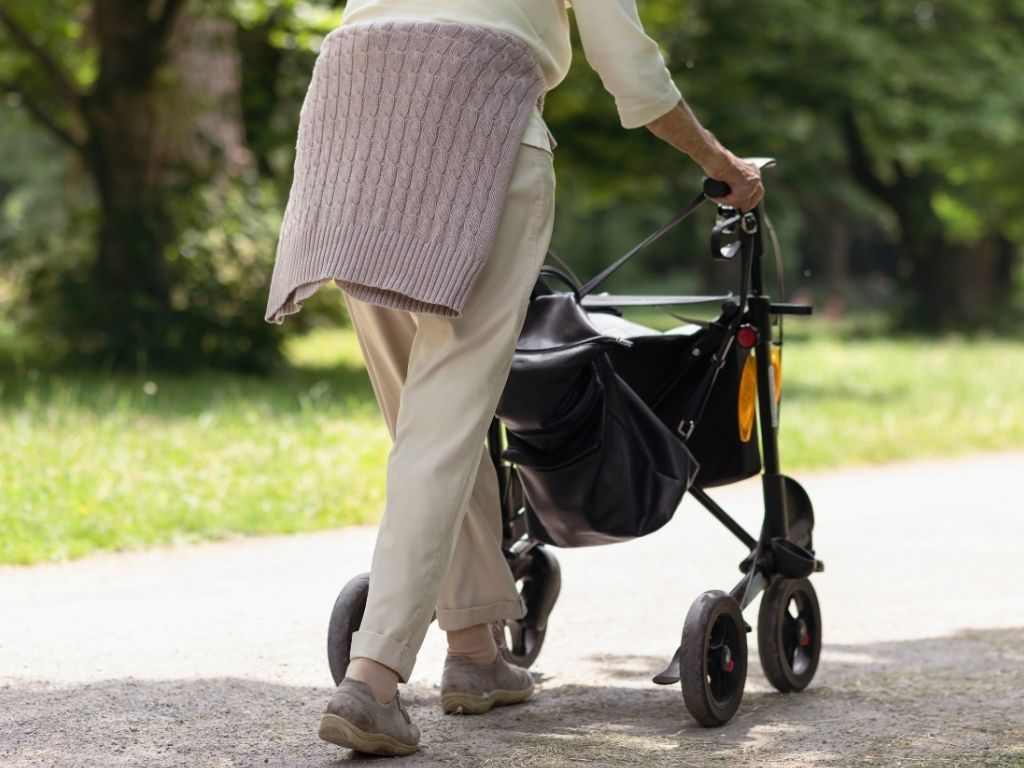 Elderly person walking along a path with a walking aid, rollator, on a sunny day