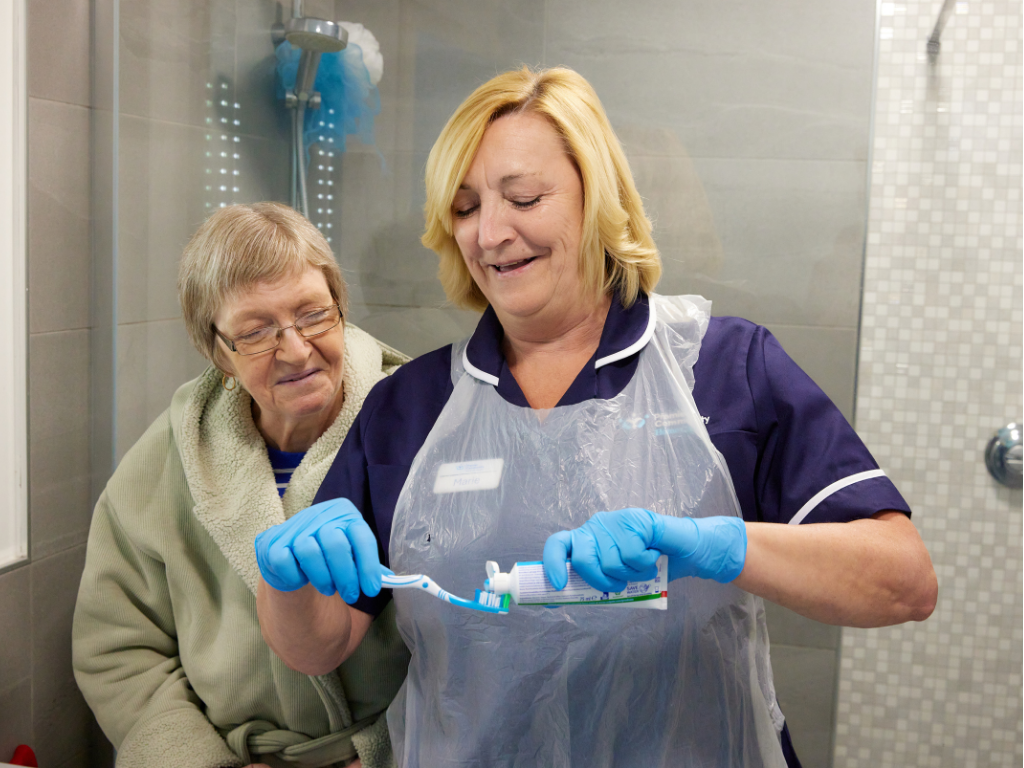 Care professional placing tooth paste on toothbrush for service user