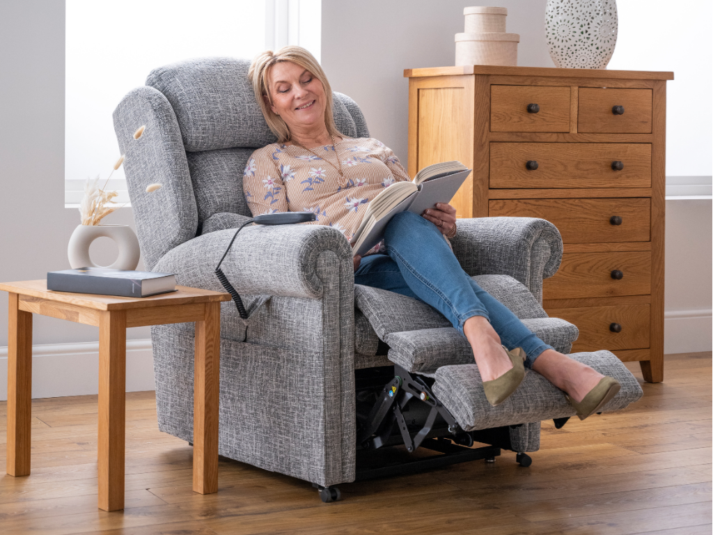 lady sat in riser recliner reading a book smiling