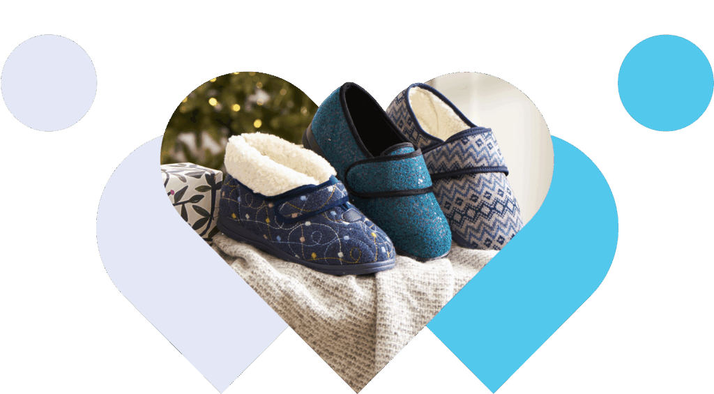 Three pairs of Cosyfeet slippers in blue tones, arranged on a blanket with a festive background. The design conveys warmth and comfort.