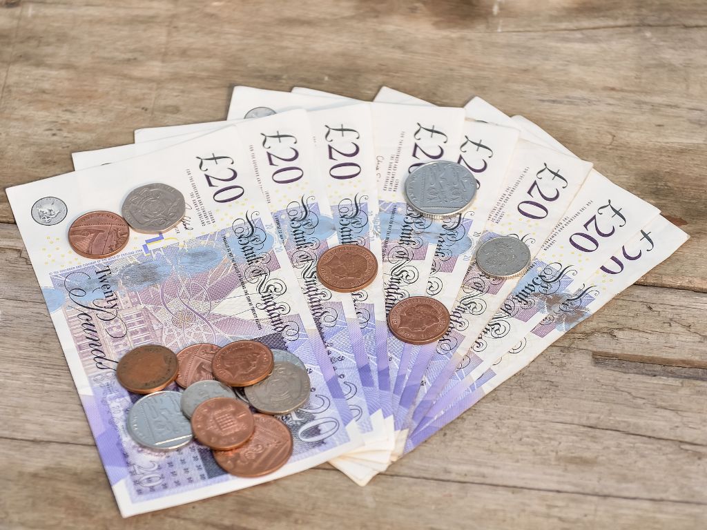 Picture of some £20 notes and change on a light wooden background