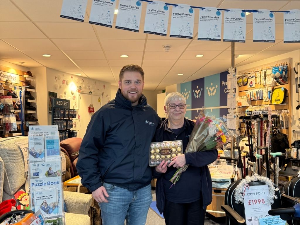 Lynne smiling holding chocolates and flowers next to Joe, mobility director