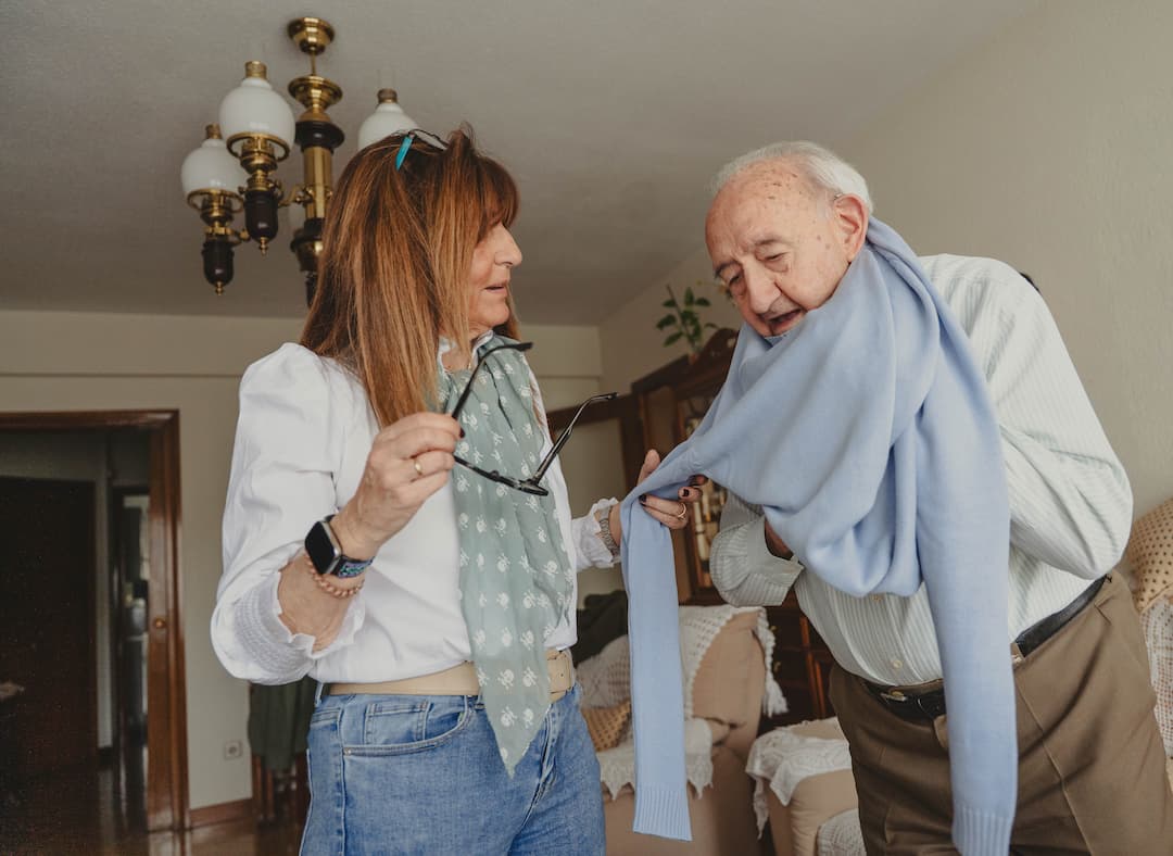 Older gentleman with grown up daughter assisting getting dressed to represent planning for future care needs