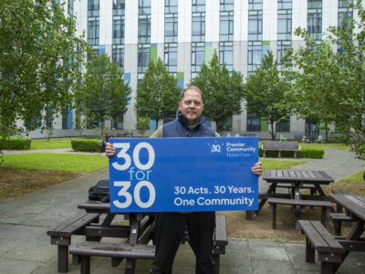 Premier Community's CEO holding a large banner advertising the company's 30for30 campaign.