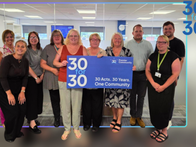 A group of people gathered around a banner that states 30for30, 30 years, 30 acts. one community.