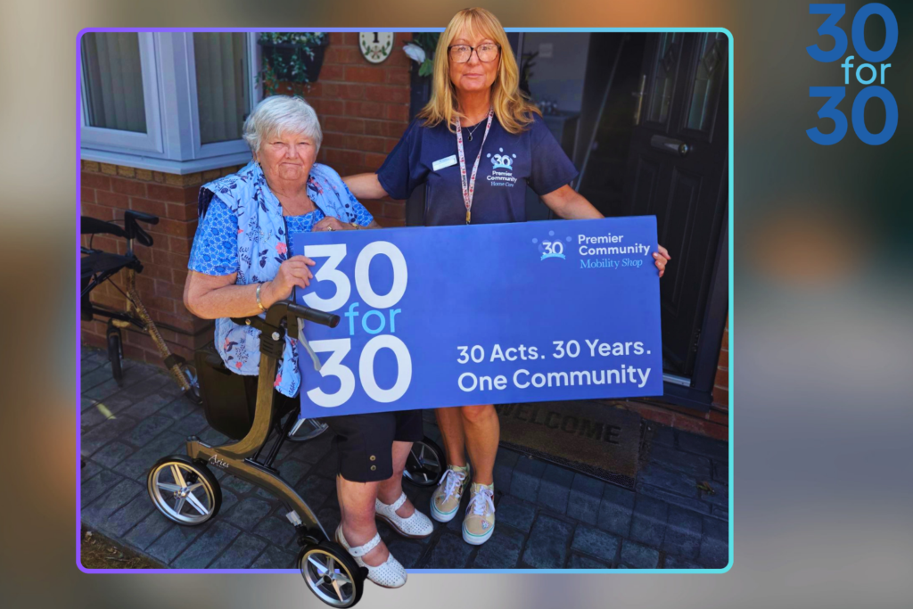 A woman sitting in a rollator with another woman standing next to her holding a banner that says 30for30, 30year, 30 acts, one community.