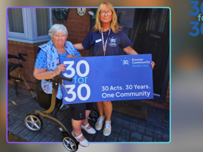 A woman sitting in a rollator with another woman standing next to her holding a banner that says 30for30, 30year, 30 acts, one community.